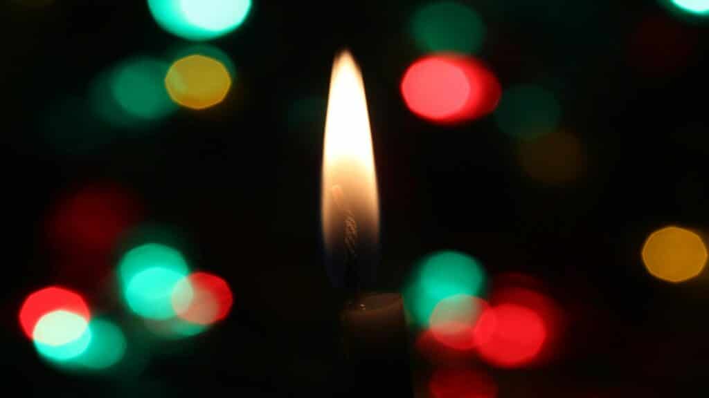 A glowing candle flame with colorful bokeh lights in the background.