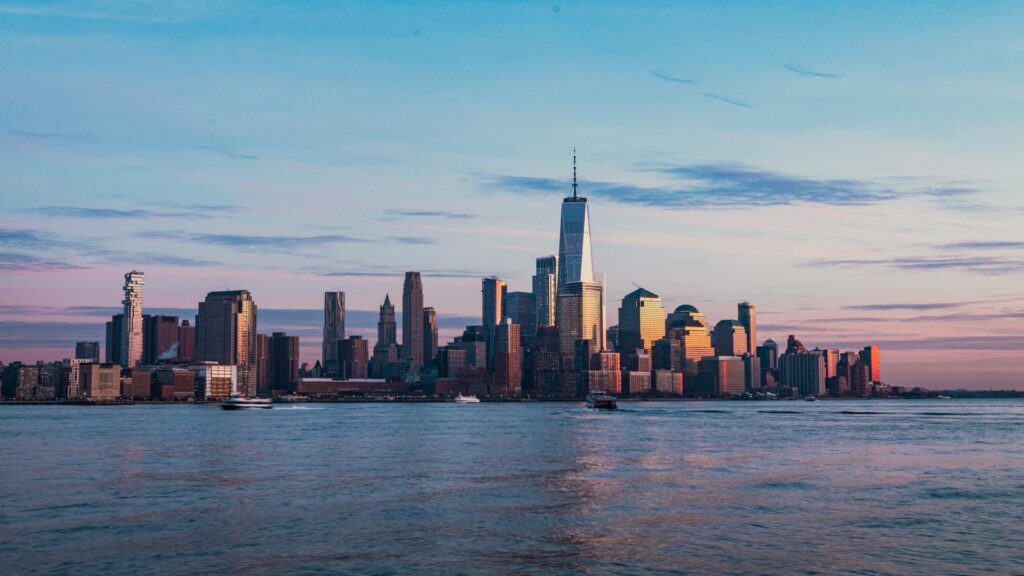 Skyline of a city with tall buildings and a river in the foreground during sunset