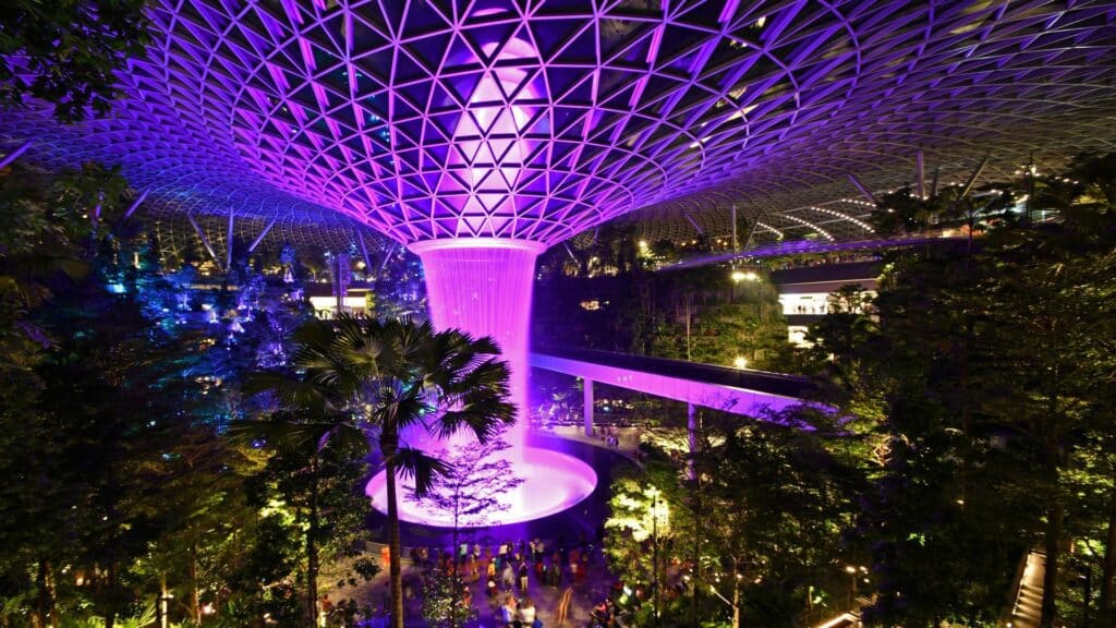 Illuminated indoor waterfall surrounded by lush greenery at night