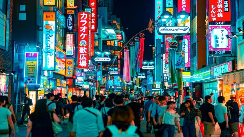 Vibrant nighttime street scene in Tokyo with neon signs, karaoke establishments and crowded streets