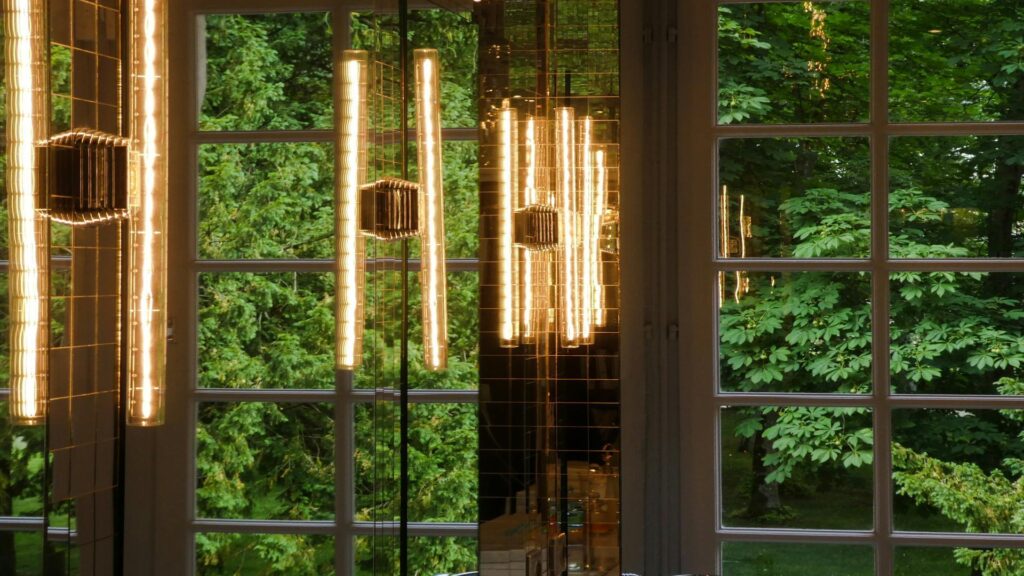 Modern vertical tube lights hanging in front of large windows overlooking lush green forest