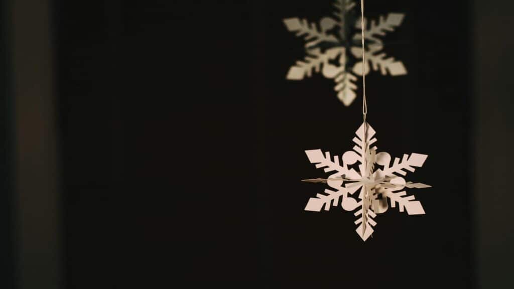 A close-up of a white paper snowflake decoration hanging against a dark background.