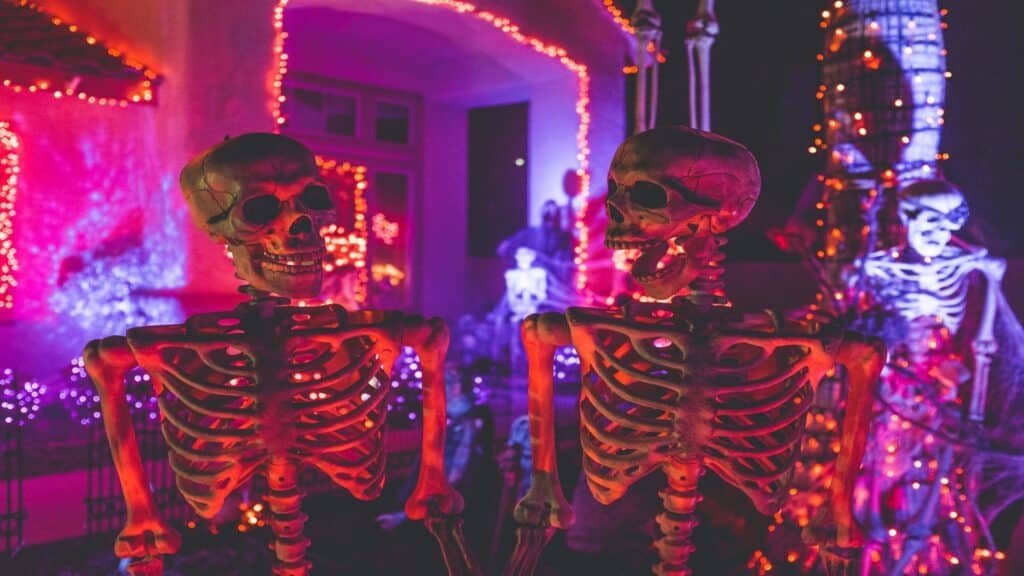 Two illuminated skeleton decorations against purple and red lighting with string lights in background