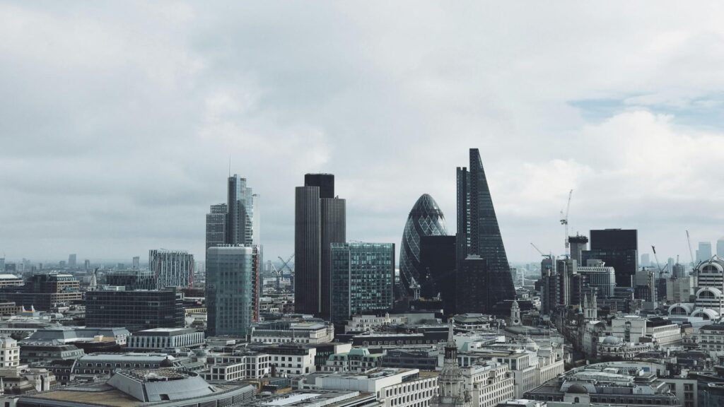 Aerial view of London's modern financial district featuring iconic skyscrapers including the Gherkin and the Leadenhall Building against a cloudy sky