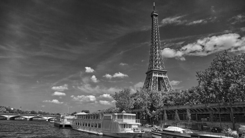 Black and white view of the Eiffel Tower with boats on the Seine River