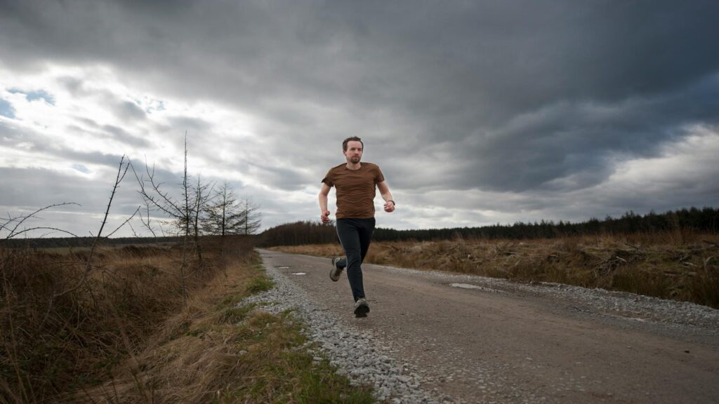 Person running on a gravel path through rural countryside under dramatic cloudy skies