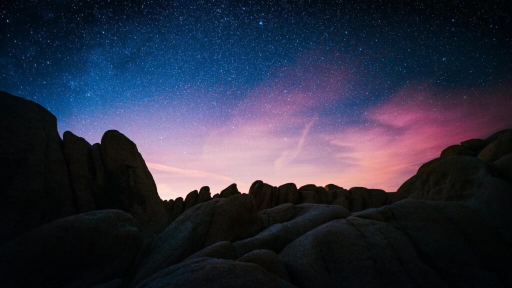 A serene night sky filled with stars above silhouetted rock formations.