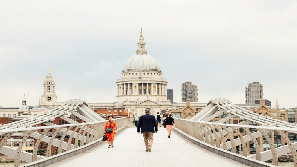 Pedestrians crossing the Millennium Bridge with St Paul's Cathedral dome in background against cloudy London sky