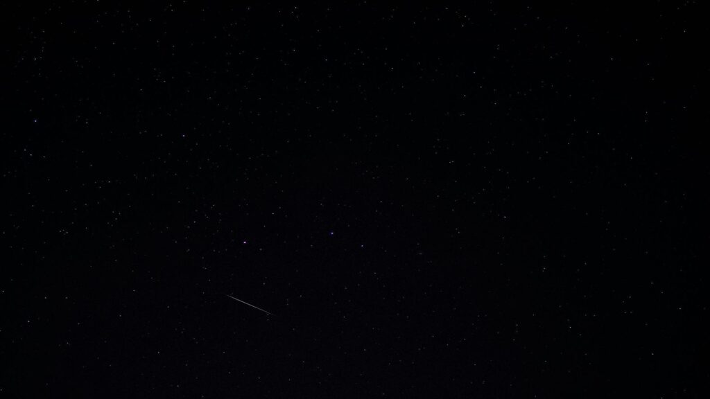 A dark night sky filled with stars and a faint shooting star streaking across.