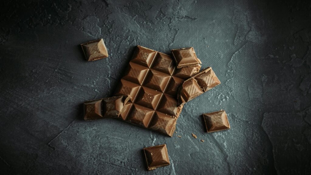 A bar of chocolate broken into pieces on a dark textured surface