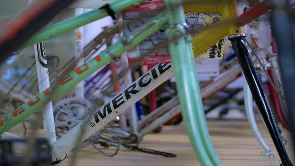 Close-up of vintage bicycle frames, including Mercier and Peugeot brands, arranged in a shop.