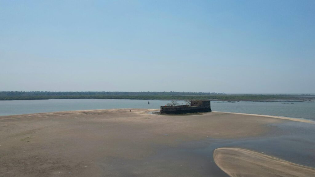 A small fort on a sandy riverbank surrounded by water under a clear blue sky.