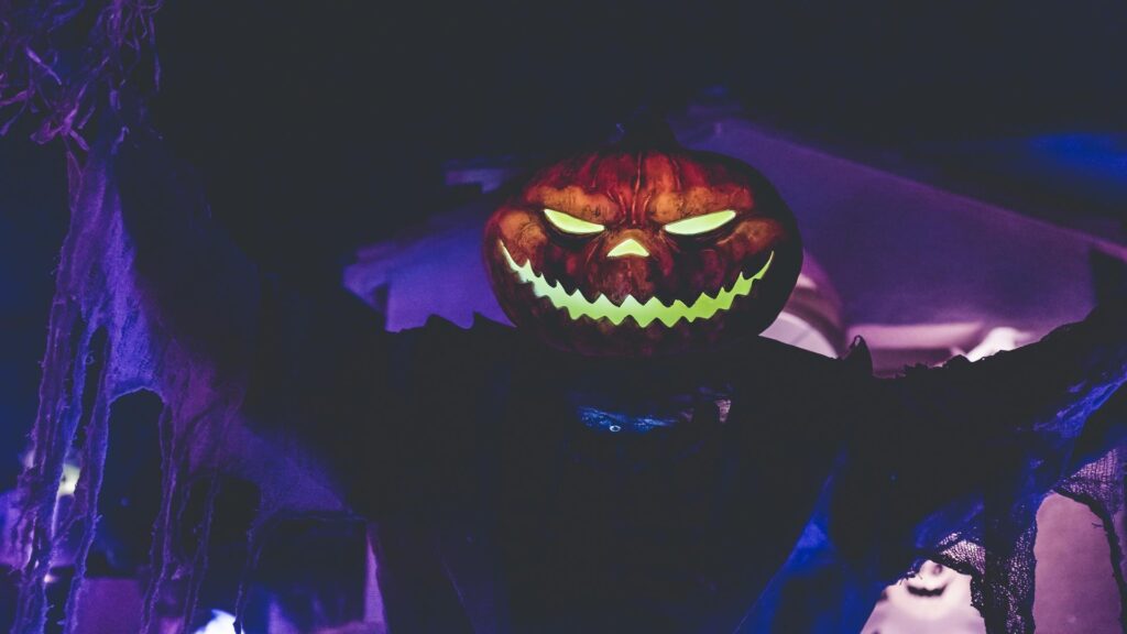 Illuminated carved pumpkin with glowing evil face against dark purple atmospheric background