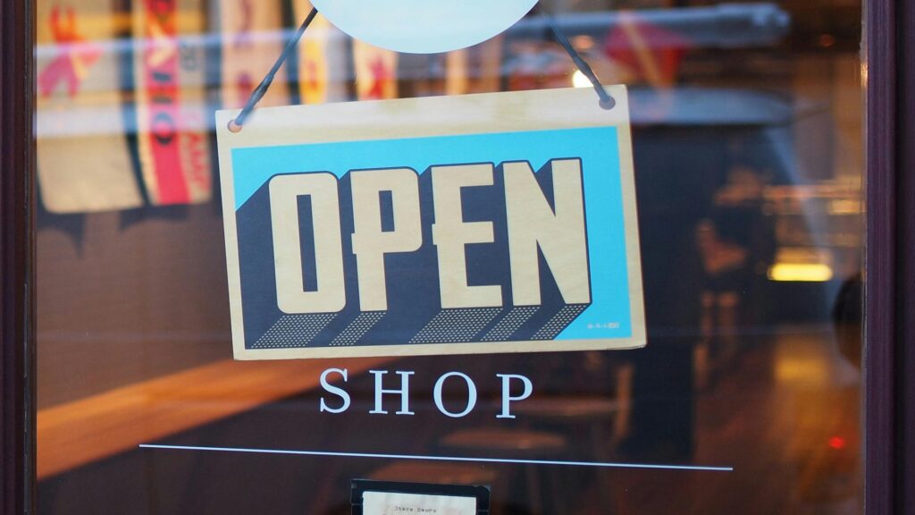 Retro-style blue and white open sign hanging in a shop window with 'SHOP' text underneath