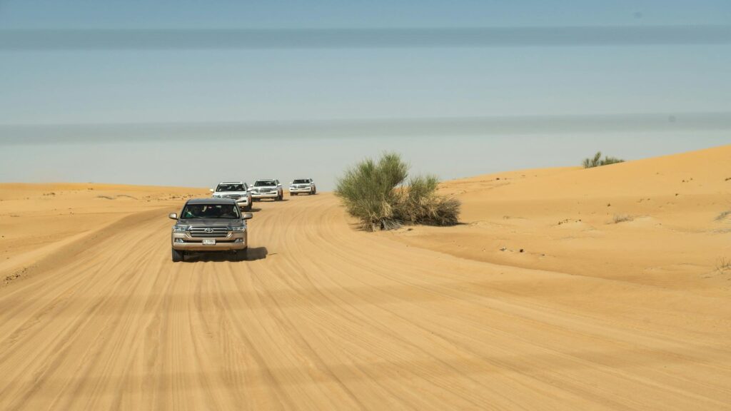 A convoy of SUVs driving through a sandy desert road.