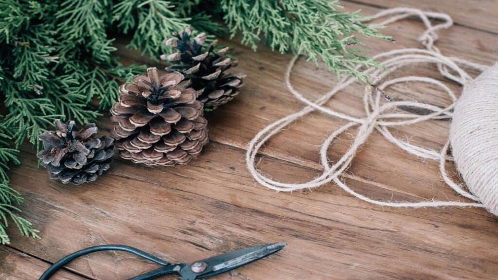 Pinecones, greenery, twine, and scissors on a wooden table.