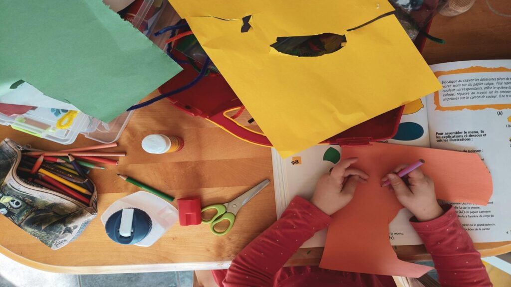 A child engaged in a colorful arts and crafts project with paper, pencils, and scissors on a table.