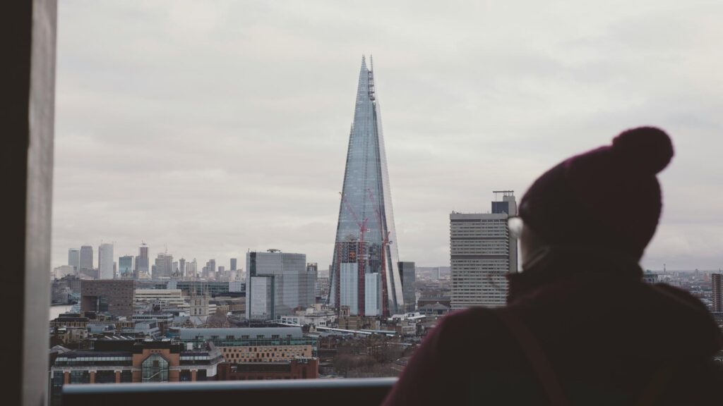 A person looking at The Shard skyscraper in London with a cloudy sky in the background.