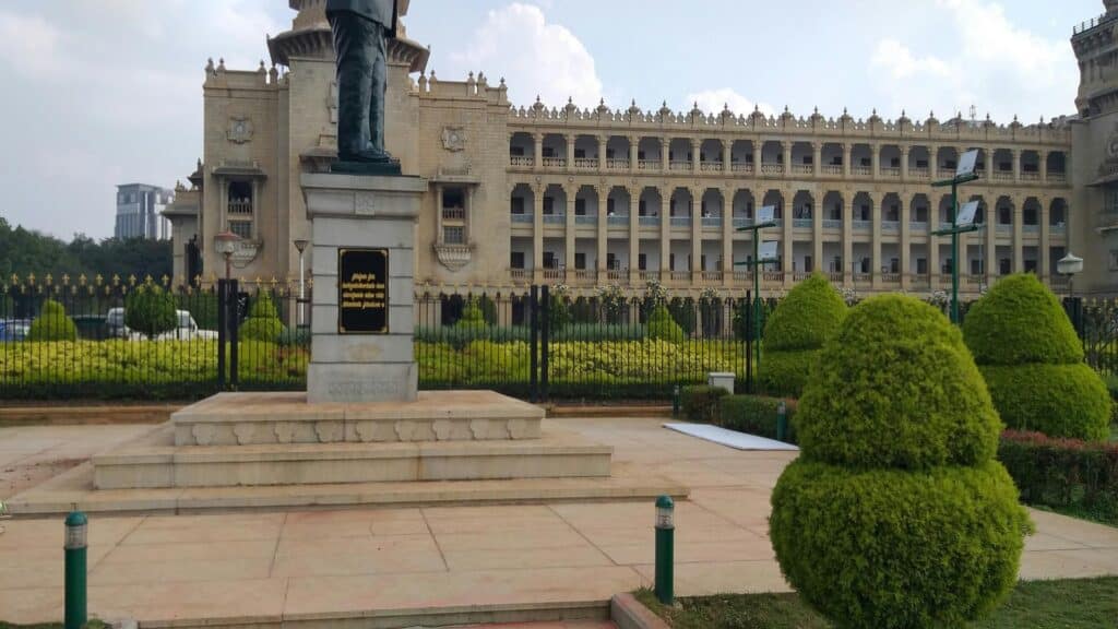 Statue in front of a grand historical building surrounded by a lush garden