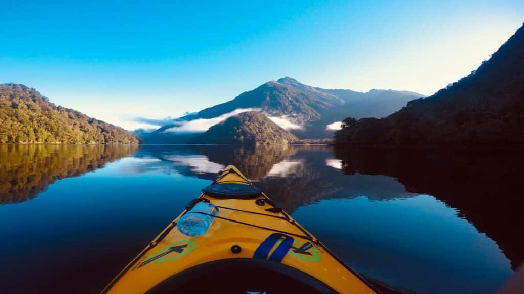 View from a kayak on a calm lake surrounded by mountains