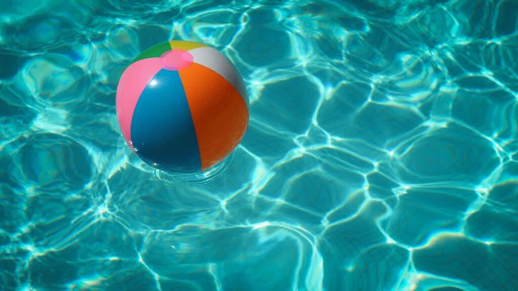 A vibrant multicolored beach ball floating on clear, rippling water in a pool.