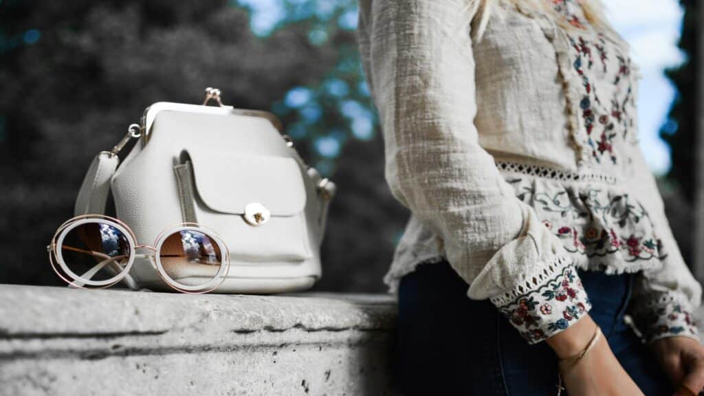 Elegant handbag and round sunglasses showcased during exhibition tours in a natural setting.