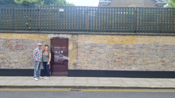 London City Attractions - Tourists at Garden Lodge entrance with historic brick wall and lattice fencing during London Taxi Tour