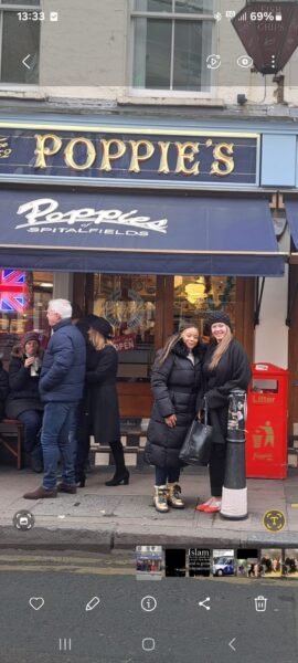 Two tourists smile outside Poppie's Fish and Chips in Spitalfields, London, highlighting a stop on Private London Tours By Car.