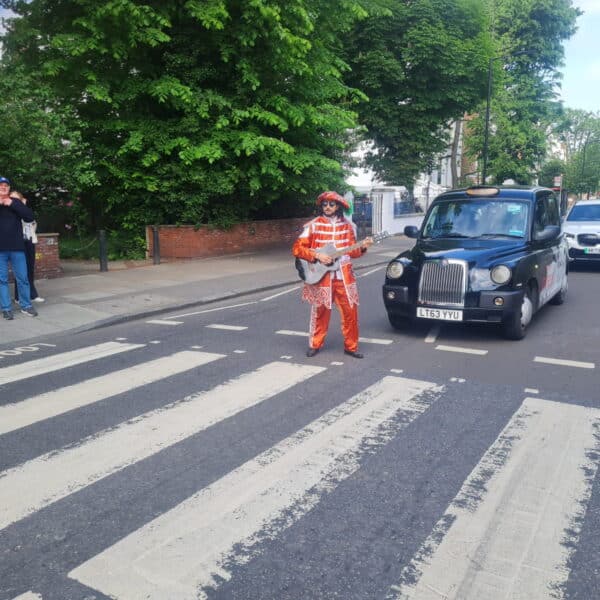 Explore London with Tours By Locals London England: A Beatles tribute artist on Abbey Road with a classic black cab.