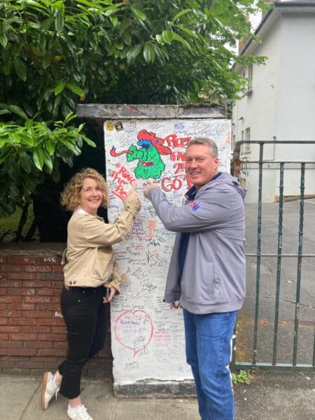 Happy couple on guided tours around London posing at iconic graffiti wall during sightseeing taxi tour experience