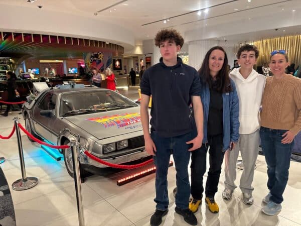 Family posing next to Back to the Future DeLorean time machine car display in shopping center