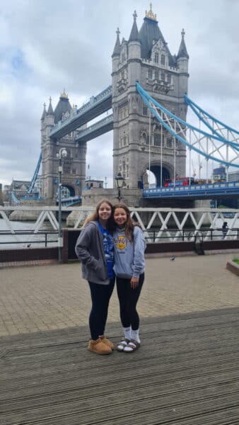 Two young women tourists posing for photo during 2 day trip to London with iconic Tower Bridge in background
