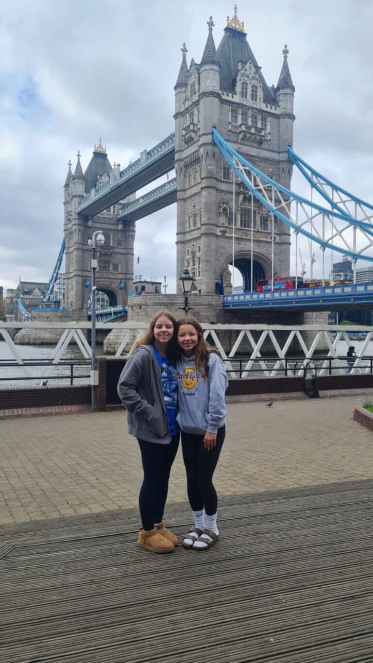 Two young women tourists posing for photo during 2 day trip to London with iconic Tower Bridge in background
