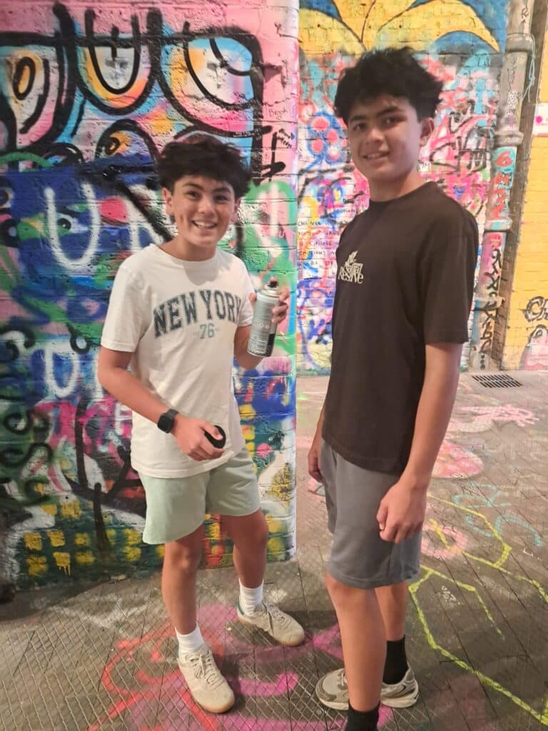 two smiling teens spray painting colorful wall during Sight See London excursion