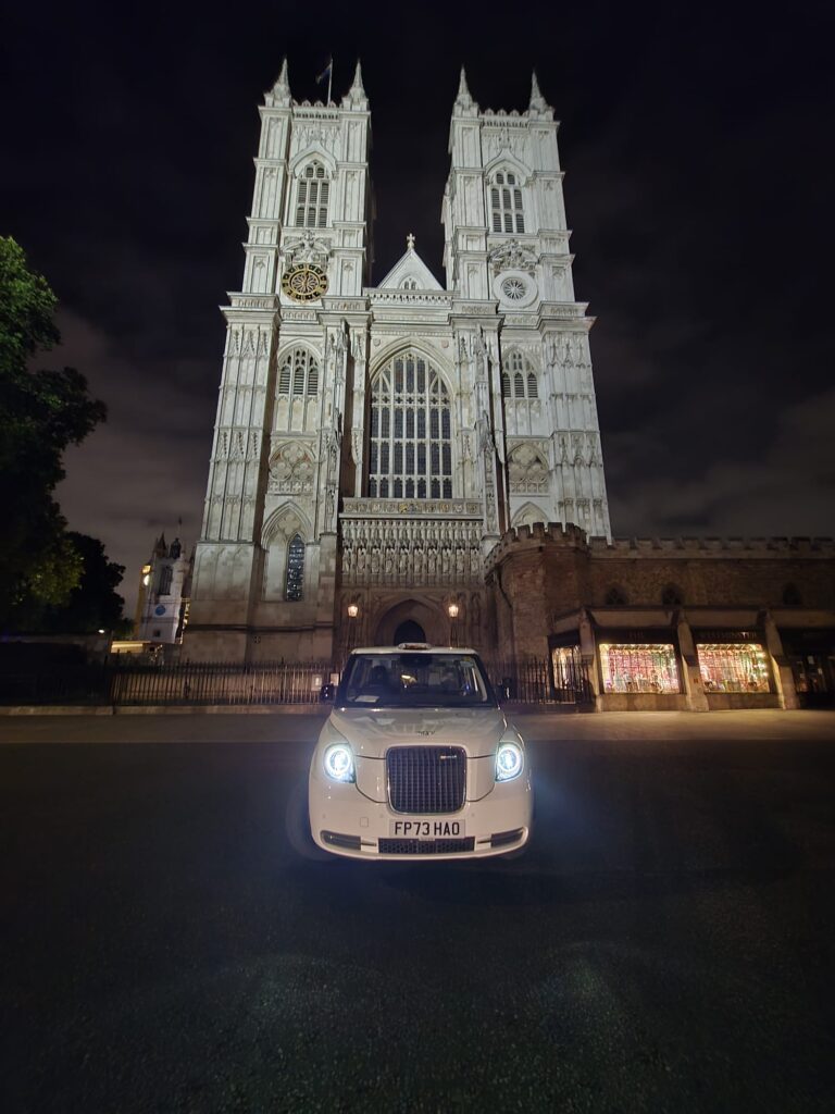Must Visit Attractions In London - Westminster Abbey illuminated at night with a London Sightseeing Taxi Tours vehicle in front