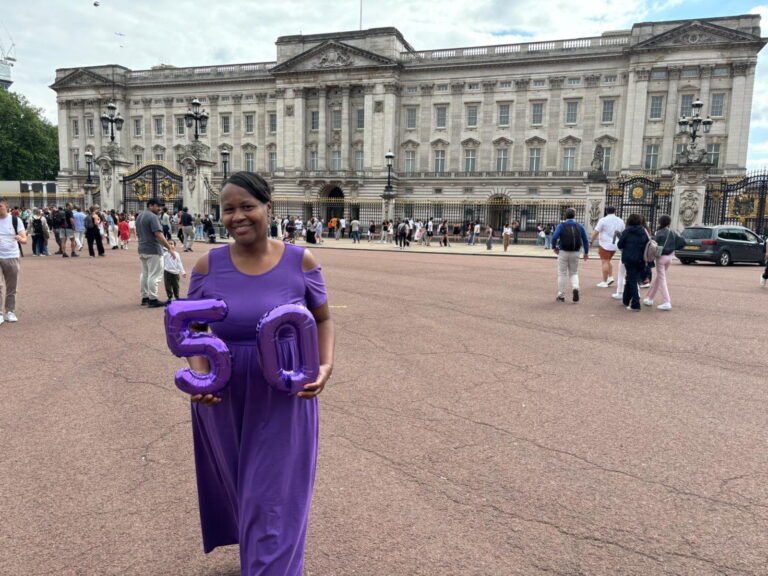 Day Trip In London Ideas - Visitor in purple dress holding '50' balloons outside Buckingham Palace, London.