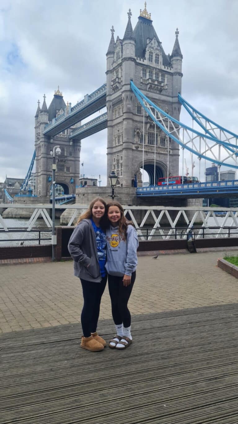 Two young visitors smiling in front of Tower Bridge during a One Day London Tour Itinerary