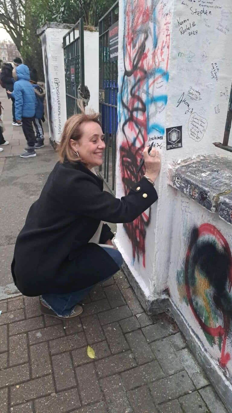 Visitor signing the famous Abbey Road wall in London, a must-see spot for those searching London New Places To Visit while on a sightseeing taxi tour.