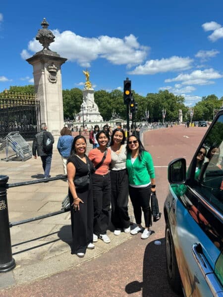 Tourists enjoying a London Best Location sightseeing taxi tour near Buckingham Palace with a classic black cab and the Victoria Memorial in the background