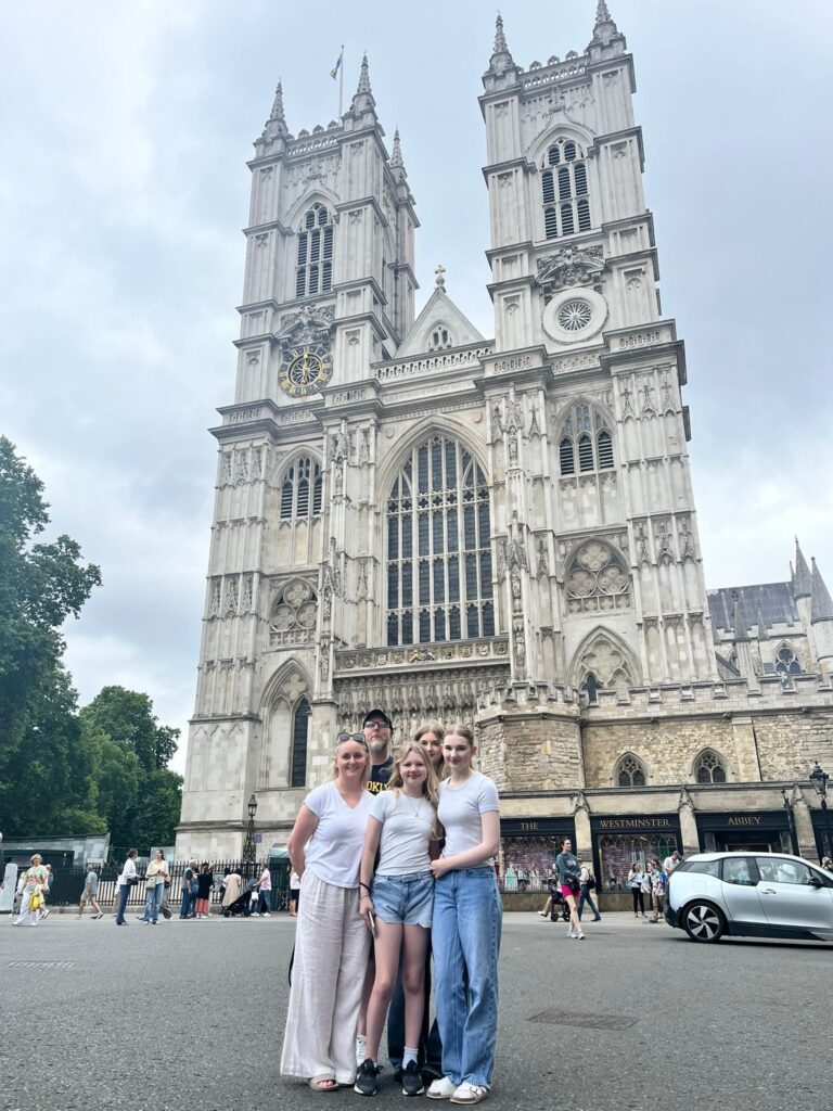 Tourists pose in front of Westminster Abbey, a must-see landmark to visit in London with London Sightseeing Taxi Tours.