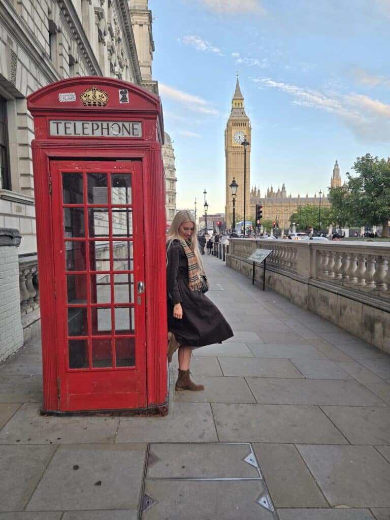 Visitor enjoying top tours in London at famous red phone booth overlooking Big Ben with London Sightseeing Taxi Tours