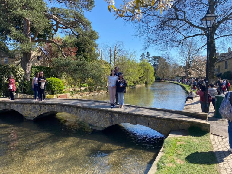 Group of tourists posing on historic stone bridge during uk tours with London Sightseeing Taxi Tours, scenic river and thatched cottages in background