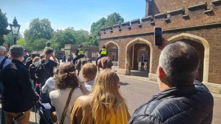 Tourists enjoying London city bus tours, viewing the iconic Changing of the Guard ceremony at Buckingham Palace with police and crowds in sunny weather