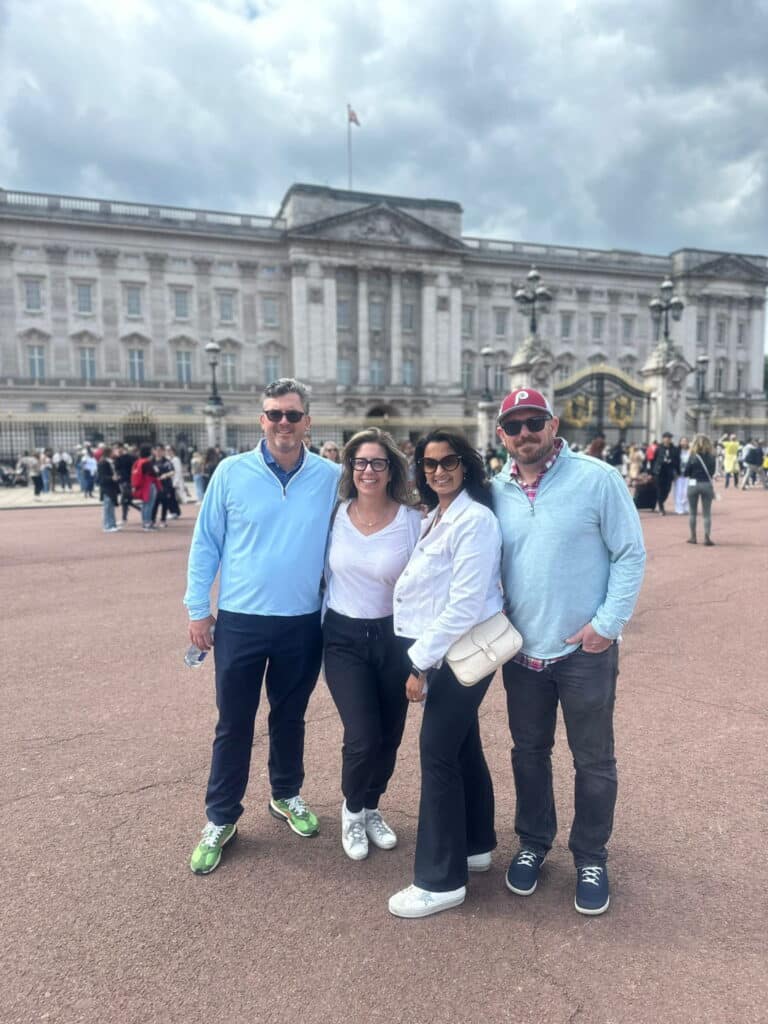 Group of tourists enjoying bus tours from London, posing in front of the iconic Buckingham Palace with cloudy skies overhead