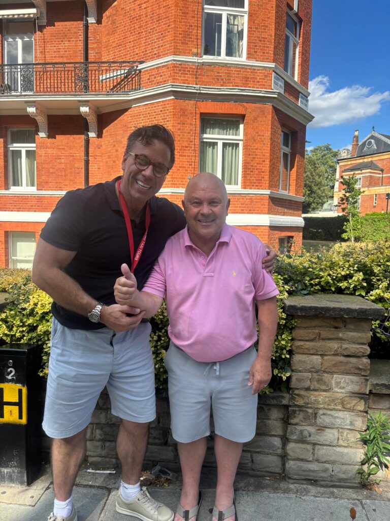two men smiling outside a red brick London building after a walking tours london taxi tour