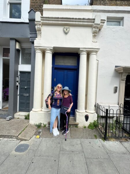 Two smiling tourists with a london tour guide outside a blue door in London