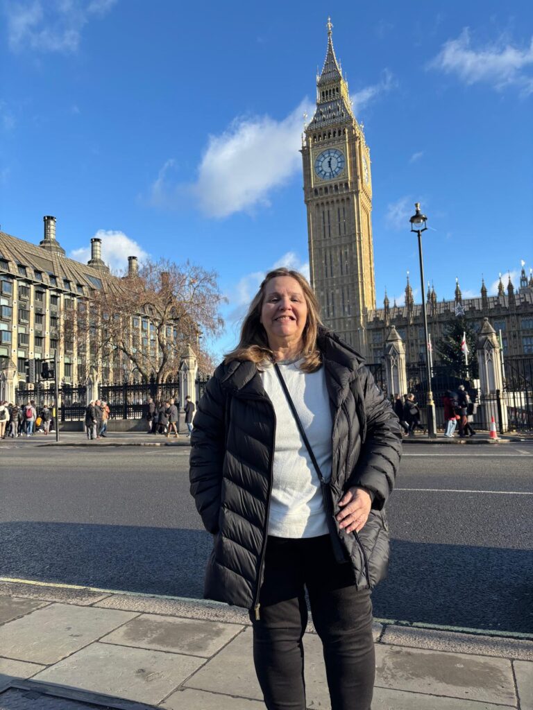 A visitor smiling in front of Big Ben during private London tours by car with London Sightseeing Taxi Tours, offering wheelchair-accessible vehicles for up to six people
