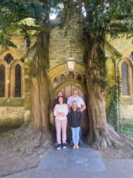 Group enjoying premium tours Stonehenge and ancient sites with London Sightseeing Taxi Tours, family posing by ancient yew tree and stone church entrance