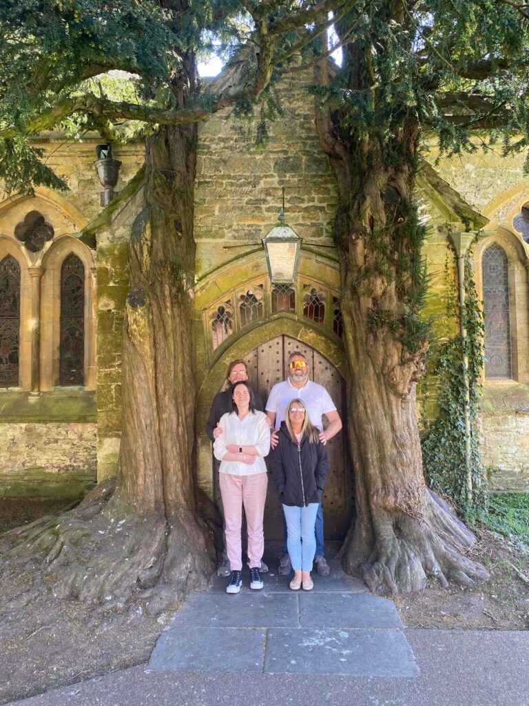 Group enjoying premium tours Stonehenge and ancient sites with London Sightseeing Taxi Tours, family posing by ancient yew tree and stone church entrance