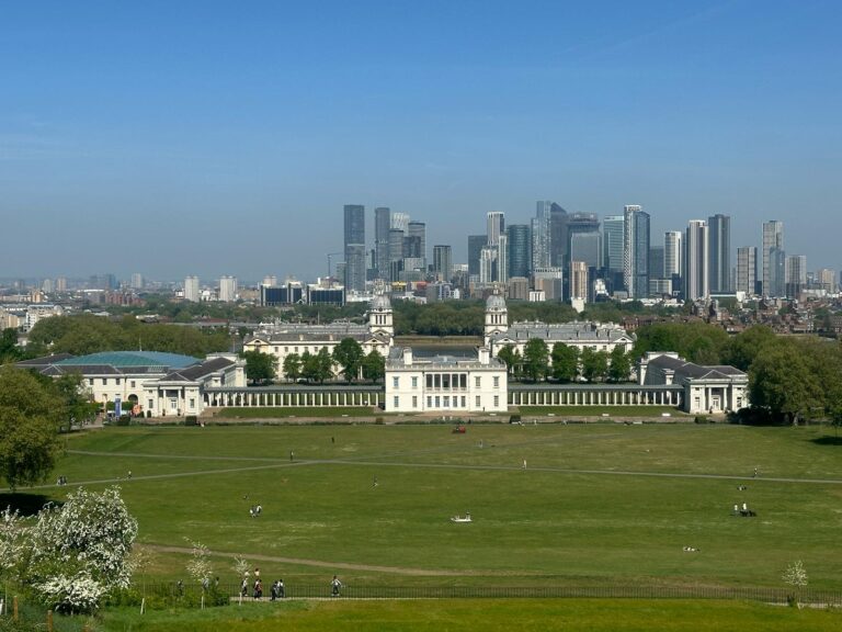 Top Things To Do In Central London - Visitors enjoying the expansive green space of Greenwich Park with the historic Royal Naval College building and the modern London skyline in the background, captured during a London Sightseeing Taxi Tour.